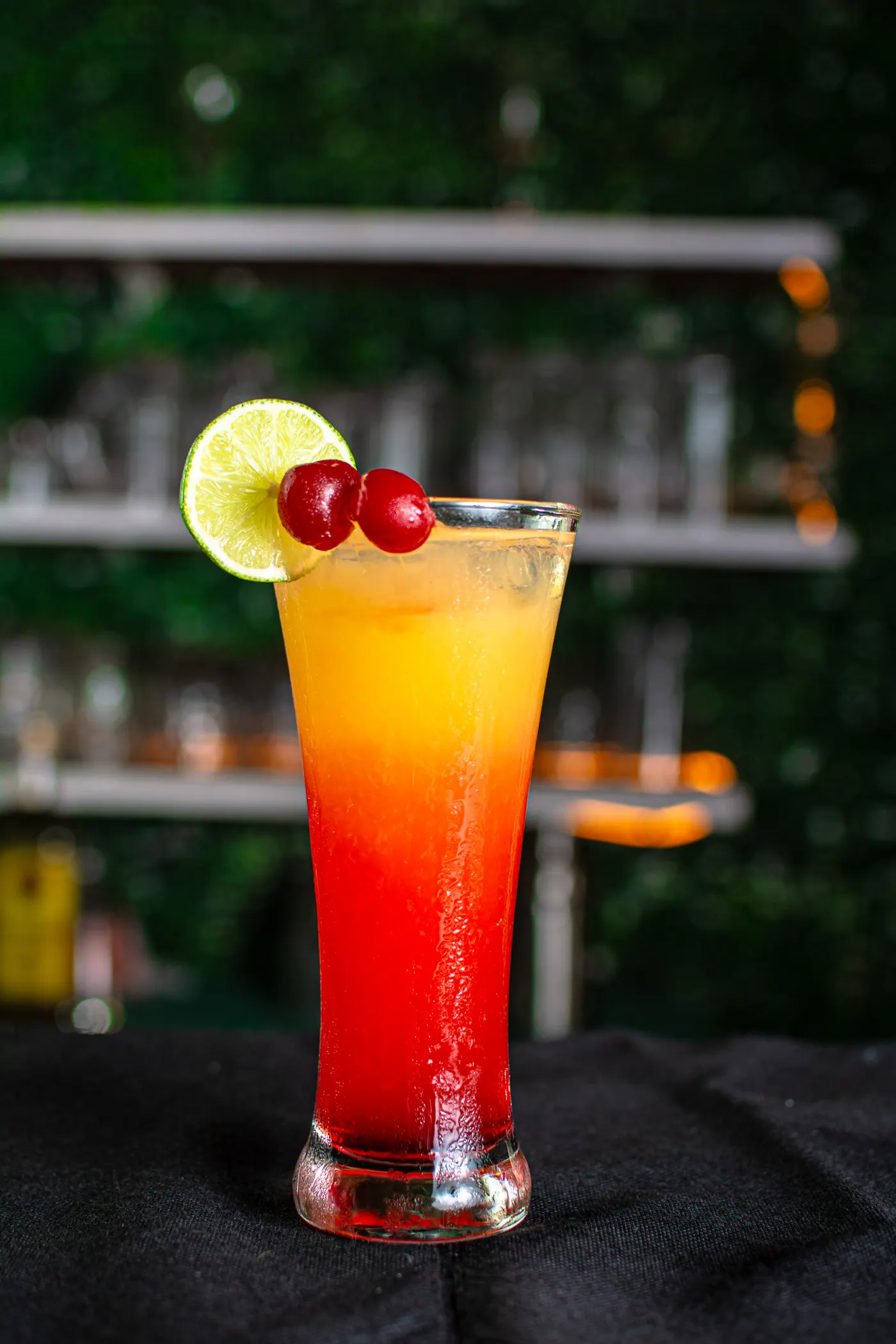 Coctel rojo y naranja con cereza y limón, frente a la barra.
