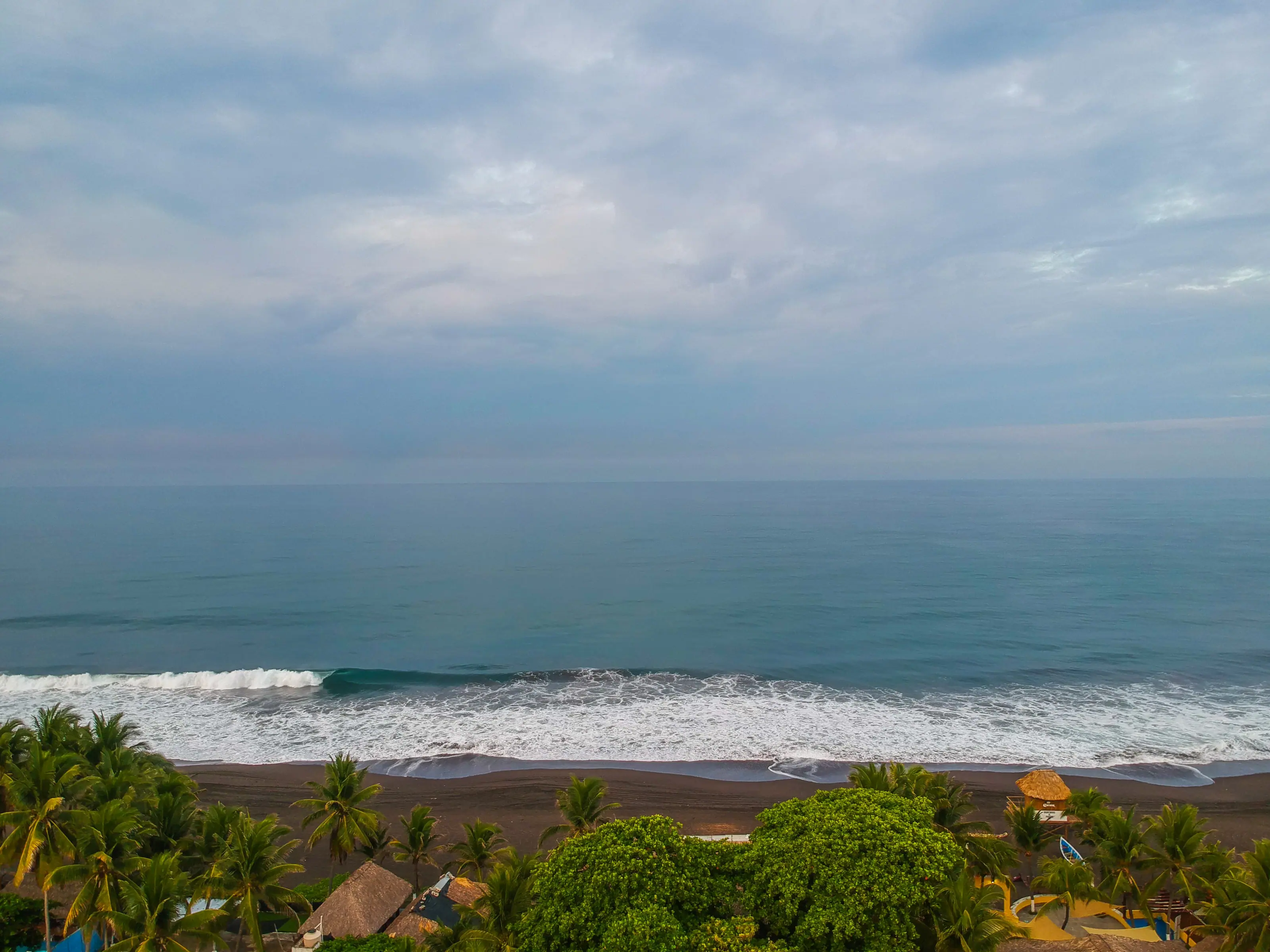 El mar de Monterrico visto desde el hotel, con la arena negra y las palmeras en primer plano.