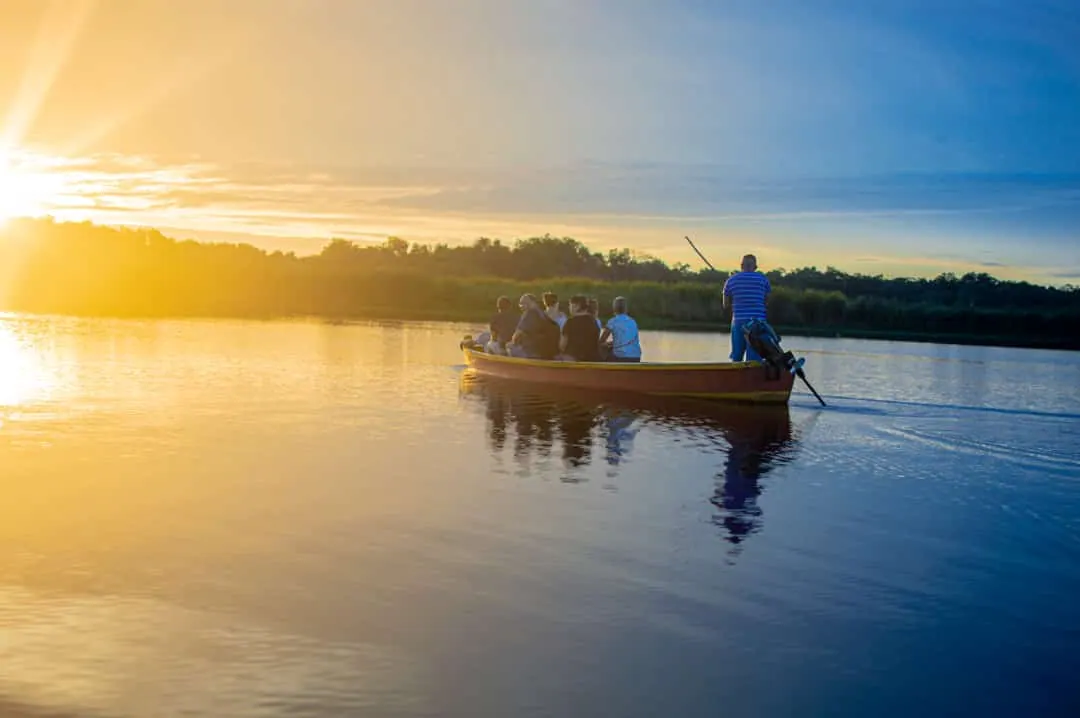 Lancha con visitantes en el Canal de Chiquimulilla, con el cielo dorado reflejado en el agua.