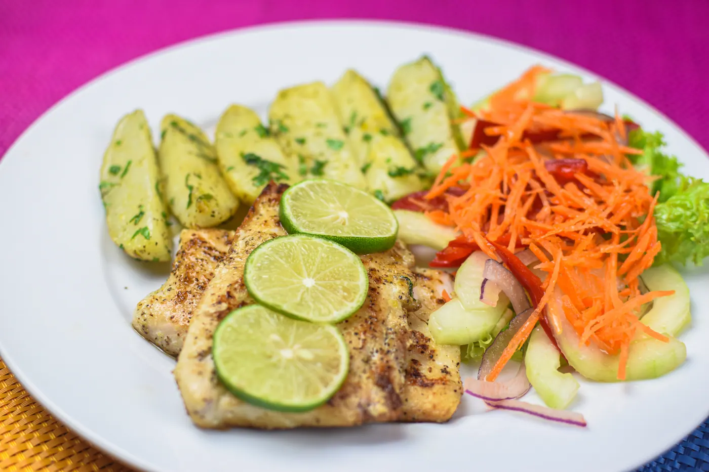 Filete de pescado con rodajas de limón, papas y ensalada.