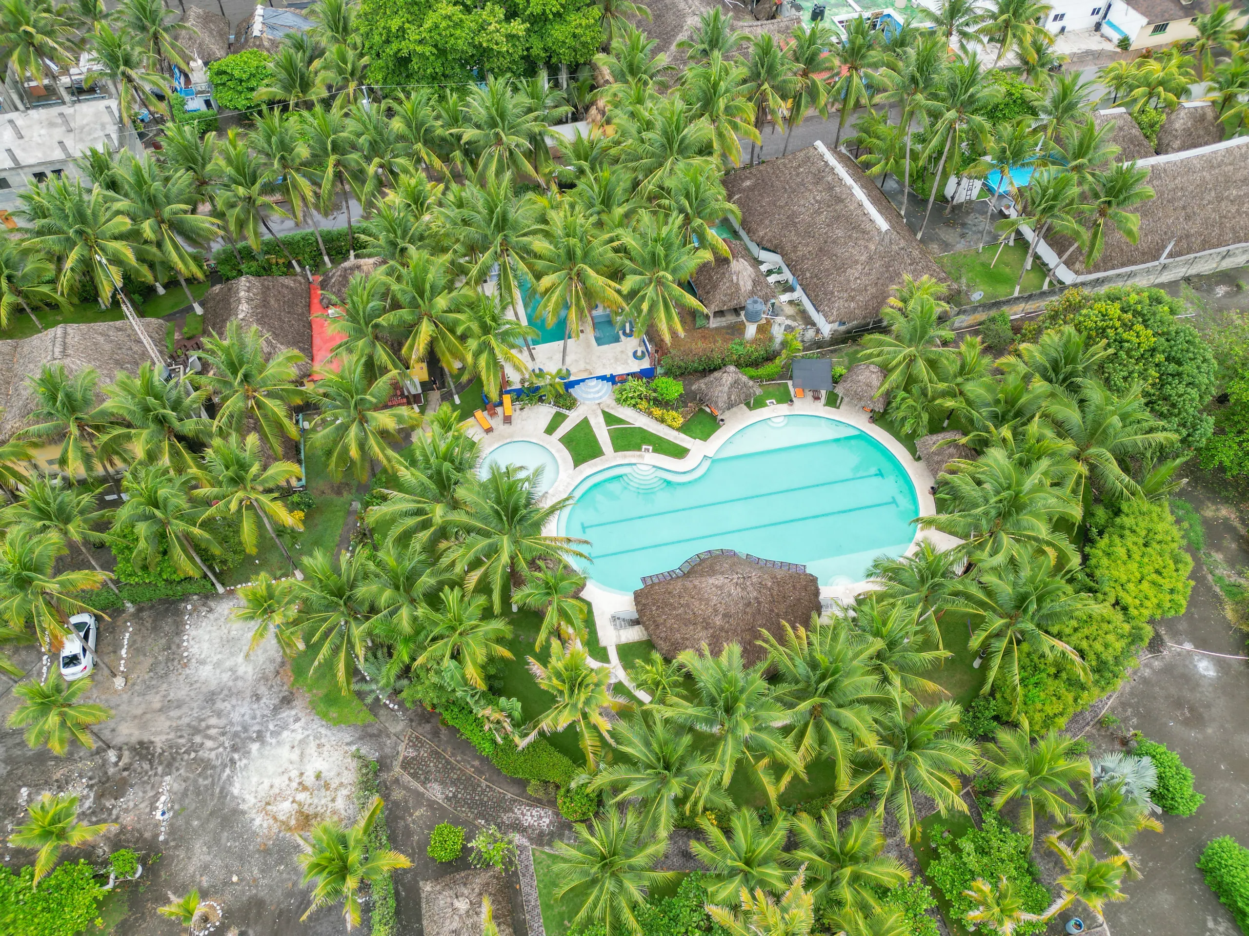 Vista aérea de la piscina del hotel rodeada de palmeras y palapas.